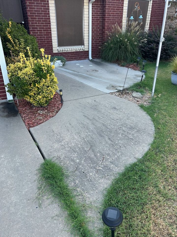 Curved concrete front walk at a red brick home, gray and streaked with dark grime, with grass growing through the joint, before cleaning
